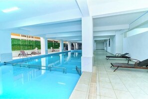 Ein Innenpool mit freiem Blick auf den Poolbereich, einige Liegestühle und eine Wand mit Grünpflanzen.