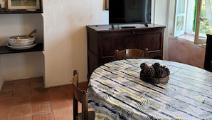A dining area with a round table covered by a leaf-patterned tablecloth, a television on a wooden cabinet, a framed picture on a shelf, and a poster on the wall. - Casa del Falco - Borgo Spigone - Vetto d'Enza - Reggio Emilia (vetto)