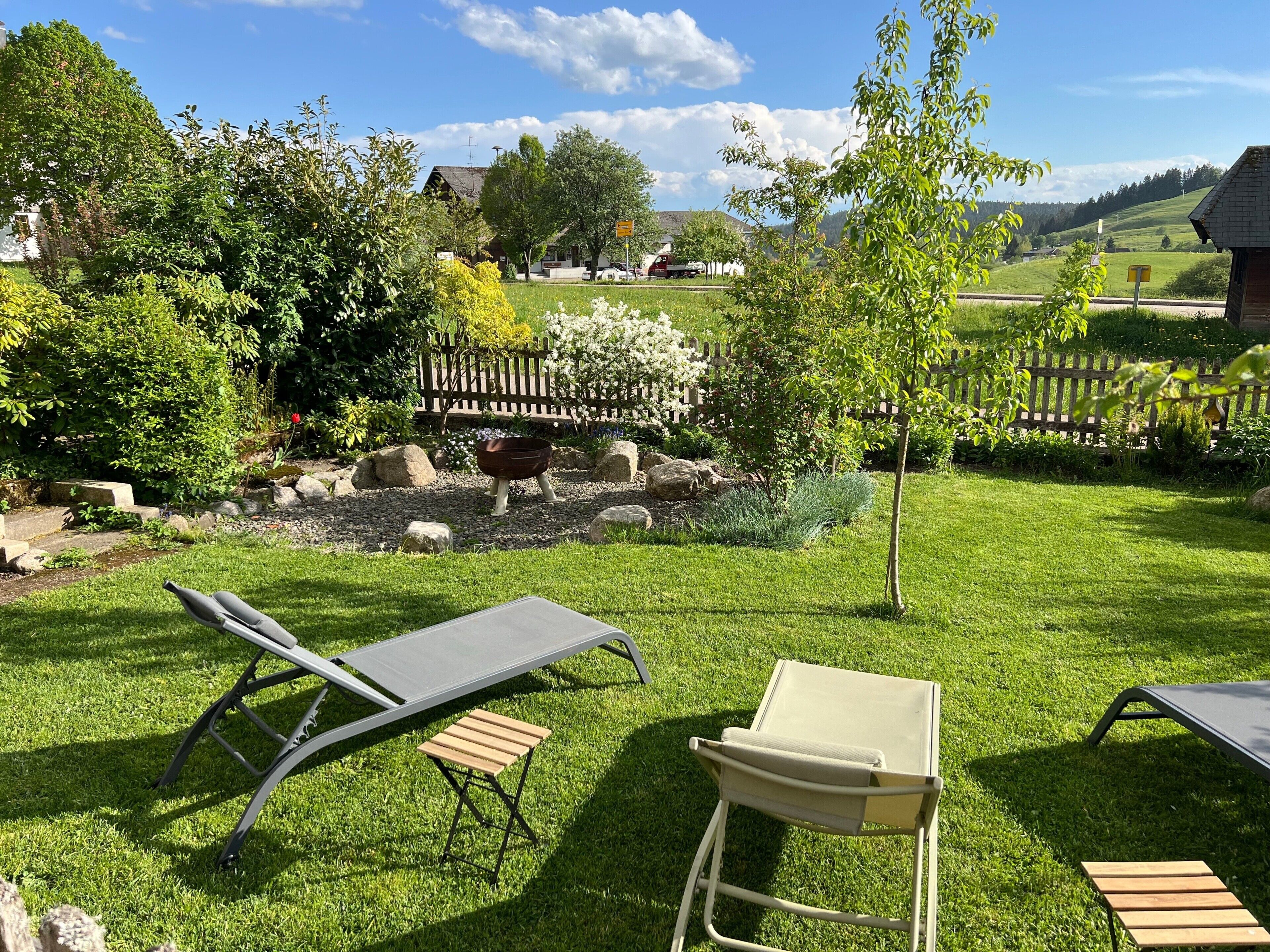 A garden with a wooden fence, a wooden bench, and a metal chair.