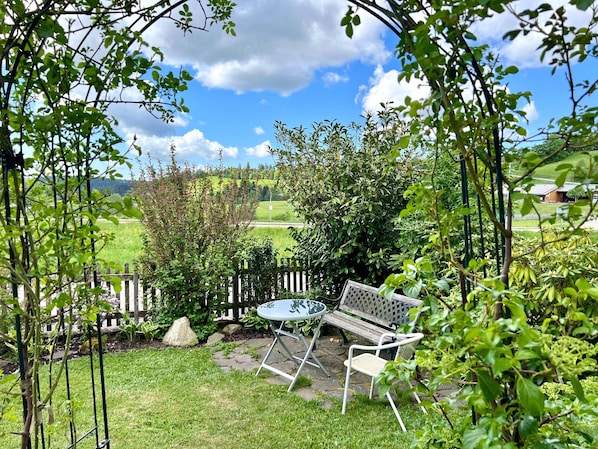A patio with a table and chairs, surrounded by greenery and a view of a rural landscape.