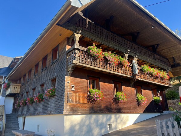 A traditional chalet with a wooden facade, multiple balconies with flower boxes, and a visible number '2' on the building.