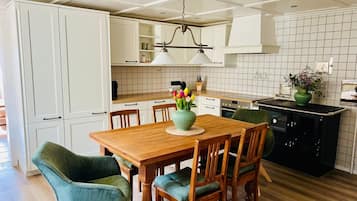 A modern kitchen with white cabinets, a wooden dining table, and green upholstered chairs.