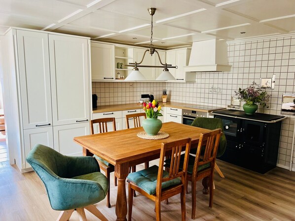 A modern kitchen with white cabinets, a wooden dining table, and green upholstered chairs.