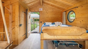 A wooden cabin room with a bed, a small table, and a chair.