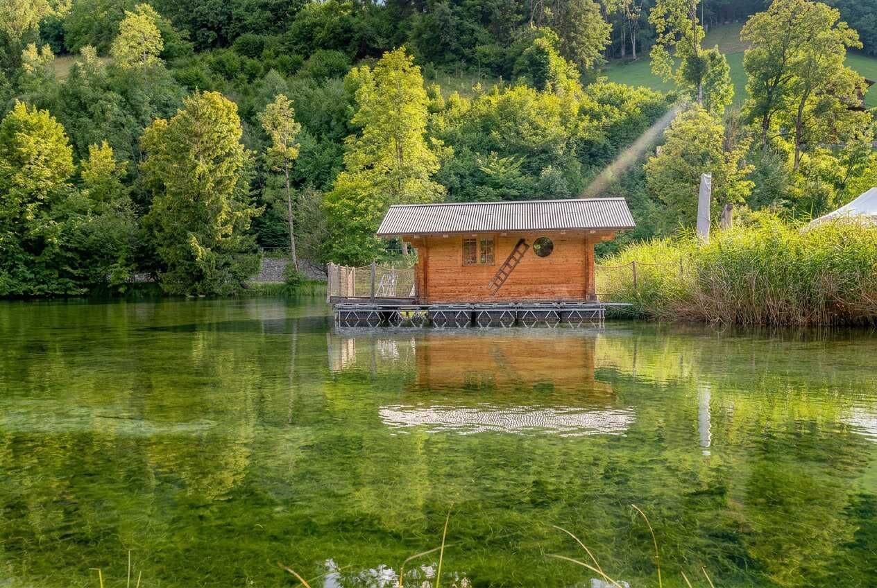 A wooden cabin on stilts over a lake, surrounded by dense forest.