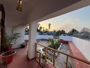 A balcony with potted plants, a railing, and a view of a residential area during sunset. - Cozy 3-bedroom Home 2 Minutes From Jambiani Beach (Jambiani)