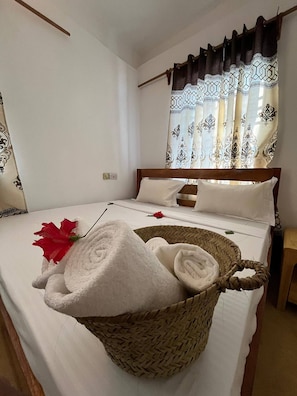 A neatly made bed with white linens, a woven basket with towels, and a red flower on the bed. - Cozy 3-bedroom Home 2 Minutes From Jambiani Beach (Jambiani)