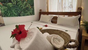 A bedroom with a bed, a wall tapestry, a curtain, and a basket with towels and flowers. - Cozy 3-bedroom Home 2 Minutes From Jambiani Beach (Jambiani)