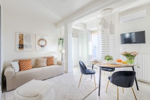A modern living room with a sofa, a dining table set for two, and a TV mounted on the wall. - Bright Panoramic Penthouse with Stunning Wrap-Around Terrace (Lucca)