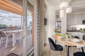 Uma sala de jantar com uma mesa posta para dois, cozinha ao fundo e vista para a cidade através de uma porta de vidro.