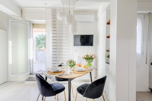 A modern dining area with a table set for two, a TV mounted on the wall, and a view of the outdoors. - Bright Panoramic Penthouse with Stunning Wrap-Around Terrace (Lucca)