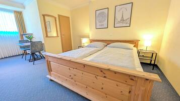 Un dormitorio con una cama de madera, un escritorio, dos lámparas de noche y dos cuadros en la pared.