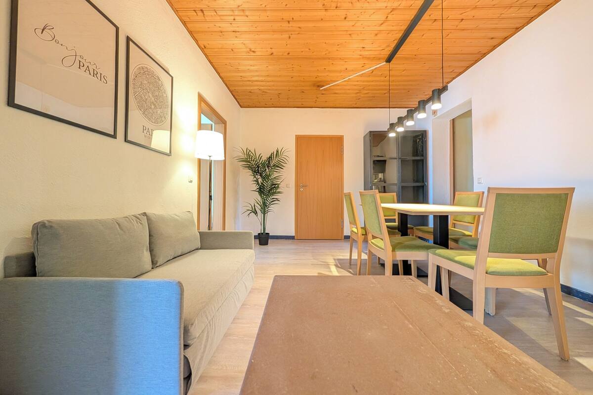 A modern living room with a sofa, a dining table with chairs, a potted plant, and framed artwork on the wall.