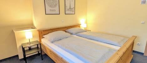 A bedroom with a wooden bed, two bedside lamps, a small table, and two framed pictures on the wall.