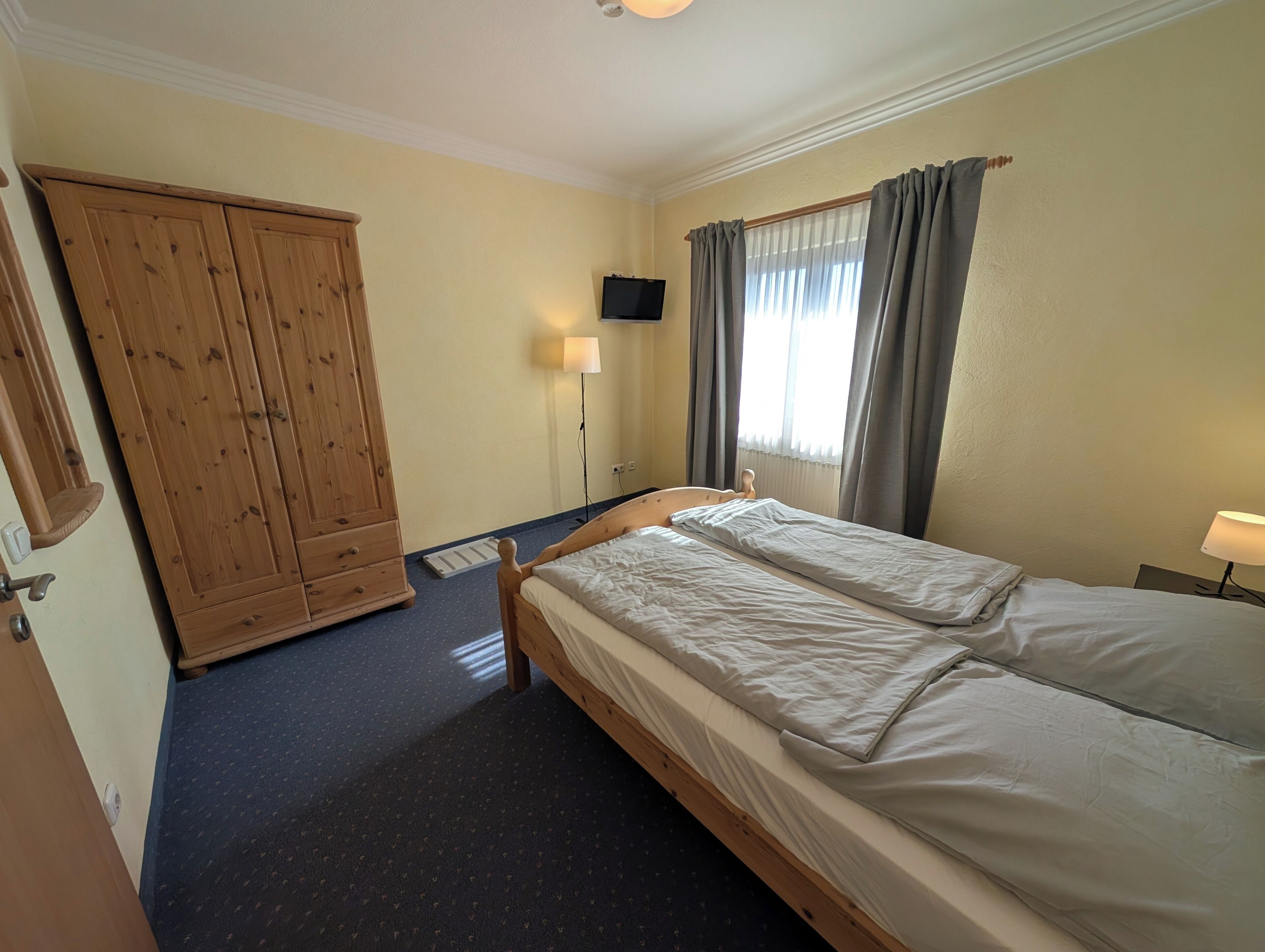 A bedroom with a bed, a wardrobe, a TV, and a window with curtains.