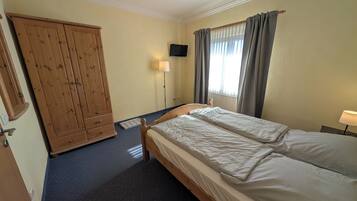 A bedroom with a bed, a wardrobe, a TV, and a window with curtains.