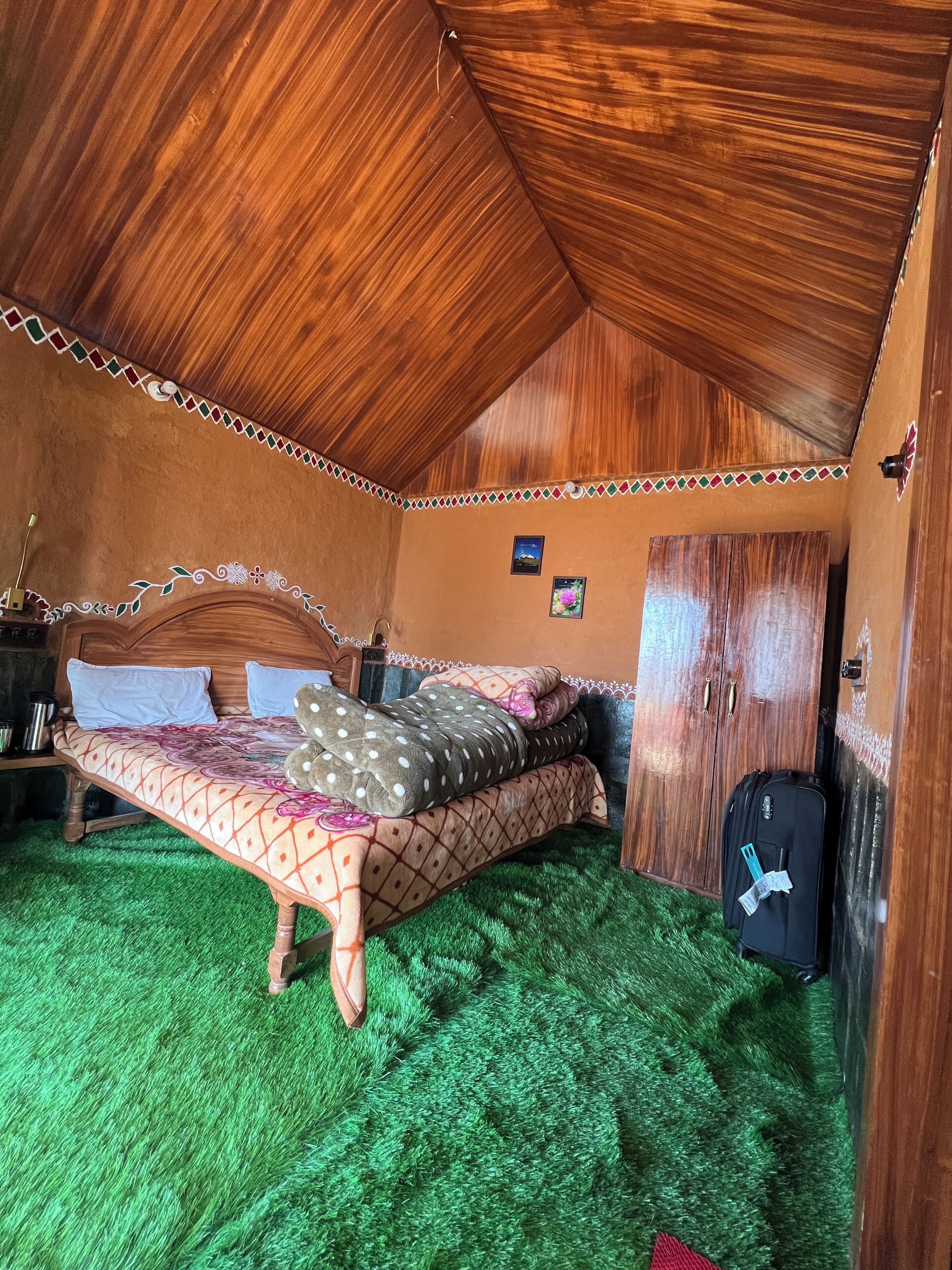 A room with a sloped ceiling, a bed with patterned bedding, a suitcase, and a small table with a lamp.