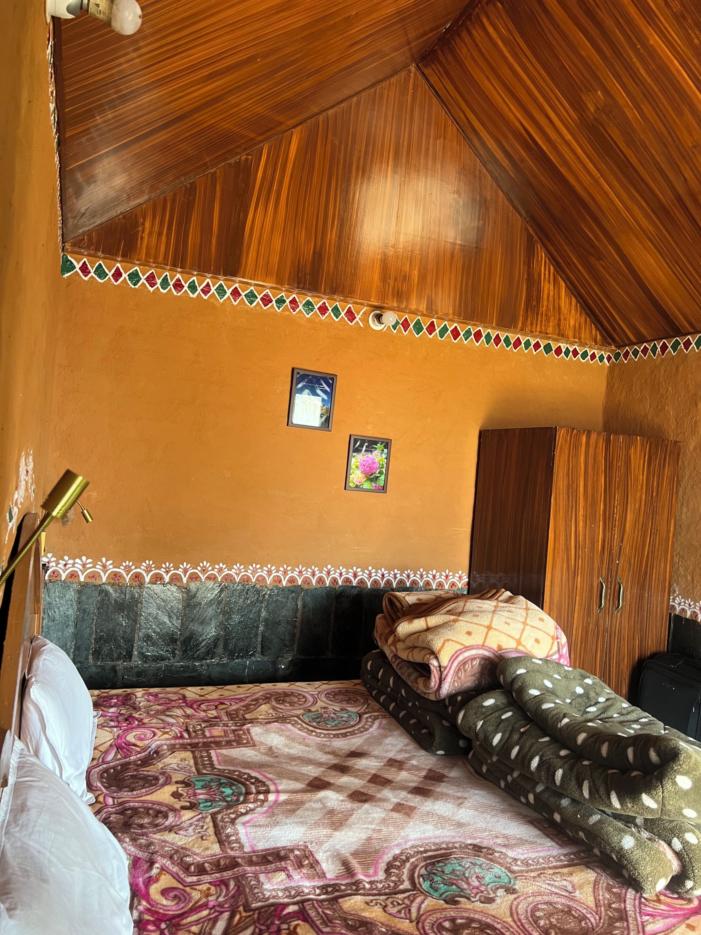 Une chambre avec un plafond en pente, un lit avec une literie à motifs, une armoire et deux tableaux encadrés accrochés au mur.