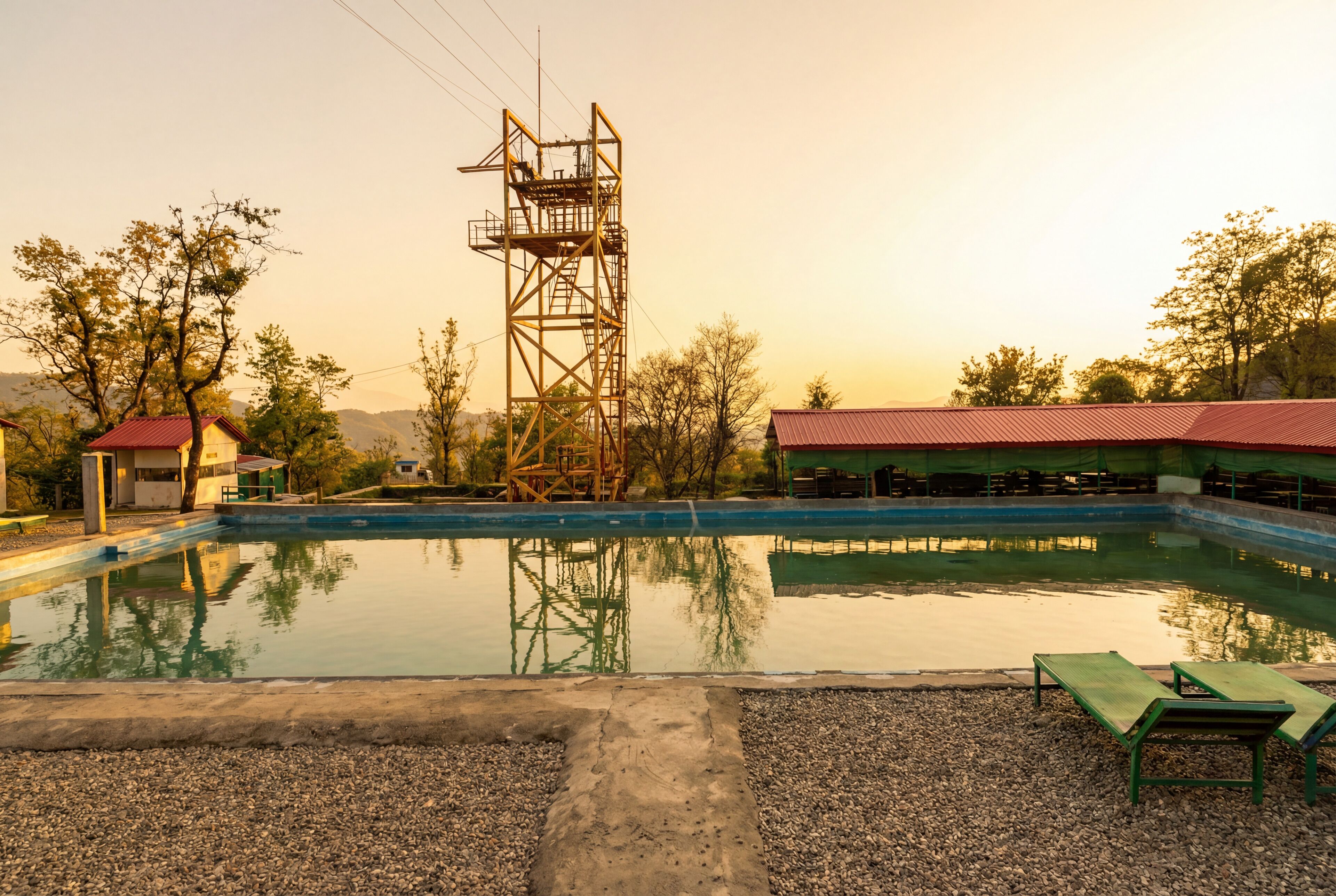 Une piscine avec une structure métallique en arrière-plan, entourée d’arbres et d’un bâtiment doté d’un toit rouge.