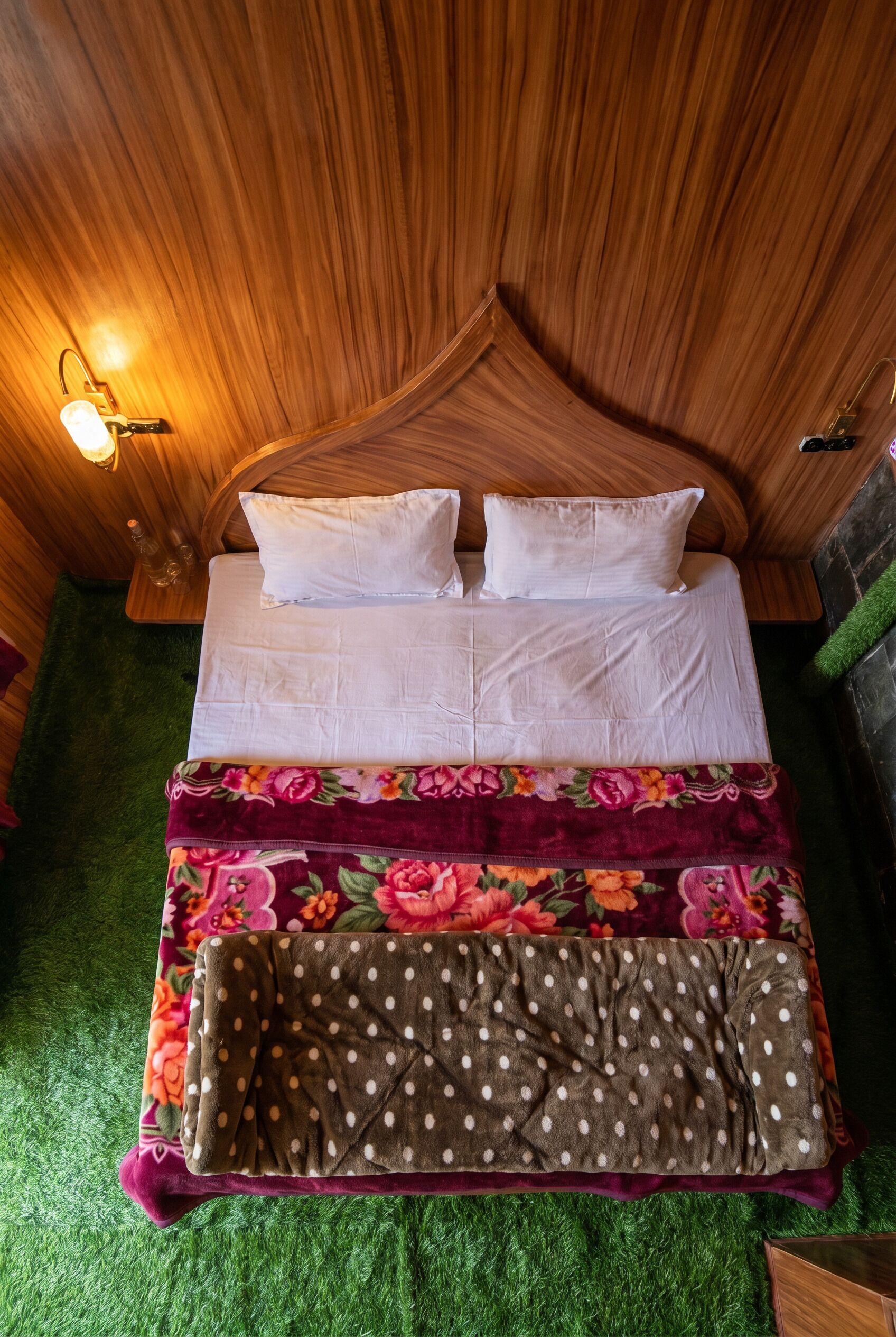 Una habitación con paneles de madera, una cama, dos luces fijadas a la pared y una alfombra verde.