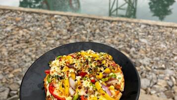 A pizza on a black plate held in front of a pool with a water slide and a tower structure in the background.