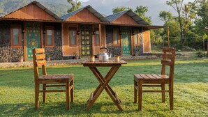 A rustic building with a stone facade, wooden doors with intricate designs, and a table with a kettle and cups. - Mhara Himachal (Bir)