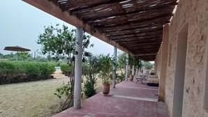 Ett takförsett utomhusområde med ett klinkergolv, krukväxter och en pergola.