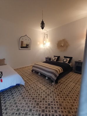 Un dormitorio con una cama, una lámpara colgante, un espejo adosado a la pared y un objeto decorativo con forma de sol.