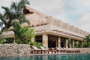 A resort with a pool area, lounge chairs, and a thatched-roof building. - Naio Hotel (Dibulla)