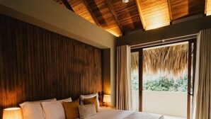 A spacious bedroom with a large bed, wooden ceiling, and a view of greenery through the window. - Naio Hotel (Dibulla)