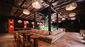 A cozy outdoor seating area with a sofa, round tables, and wicker pendant lights. - Naio Hotel (Dibulla)