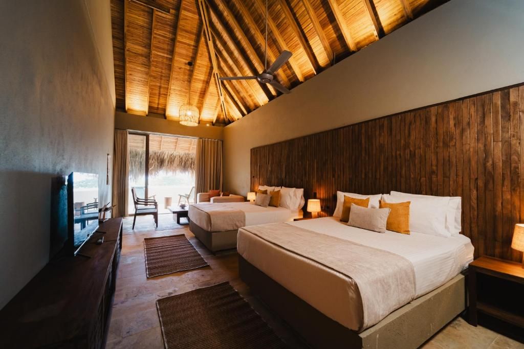 Habitación de hotel con dos camas, techo de madera, televisor y vistas al exterior.