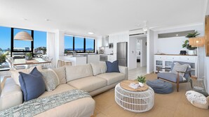 A modern living room with a sofa, coffee table, and a view of the city. - Absolute Beachfront on Albatross - SeaView 3 bed (Mermaid Beach)