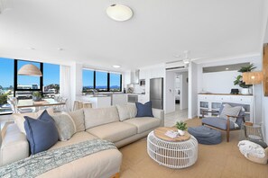A modern living room with a sofa, coffee table, and a view of the city. - Absolute Beachfront on Albatross - SeaView 3 bed (Mermaid Beach)