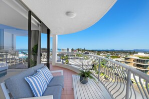 Een balkon met een bank, een bloempot en uitzicht op een stadsgezicht.