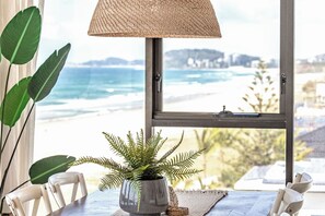 A room with a view of the ocean, a potted plant, a woven lamp, and a table with chairs. - Absolute Beachfront on Albatross - SeaView 3 bed (Mermaid Beach)