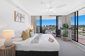 Een hotelkamer met een bed, een plafondventilator, uitzicht op de stad en een potplant.