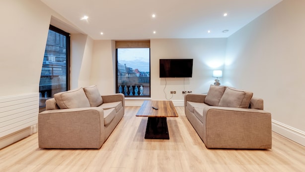 A modern living room with two sofas, a coffee table, a TV, and a window with a city view. - One by Elite  (Liverpool)