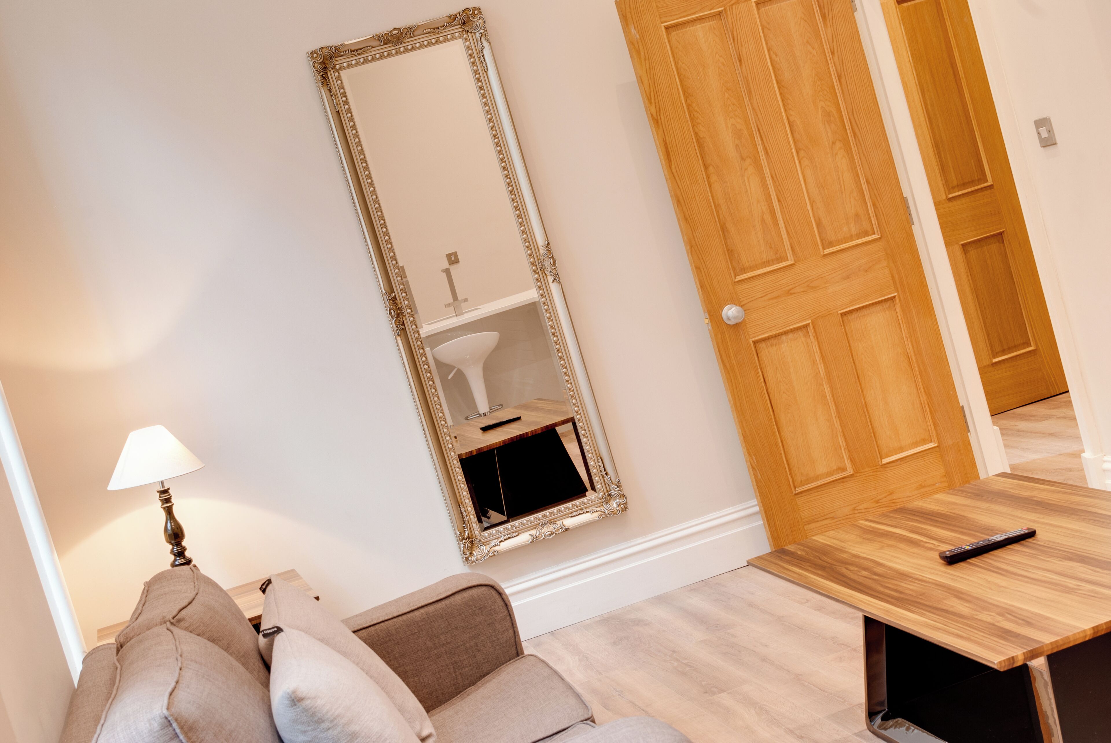 A room with a wooden door, a mirror, a lamp, and a sofa.