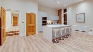 A modern kitchen with white cabinetry, a central island with bar stools, and a dining area. - One by Elite  (Liverpool)