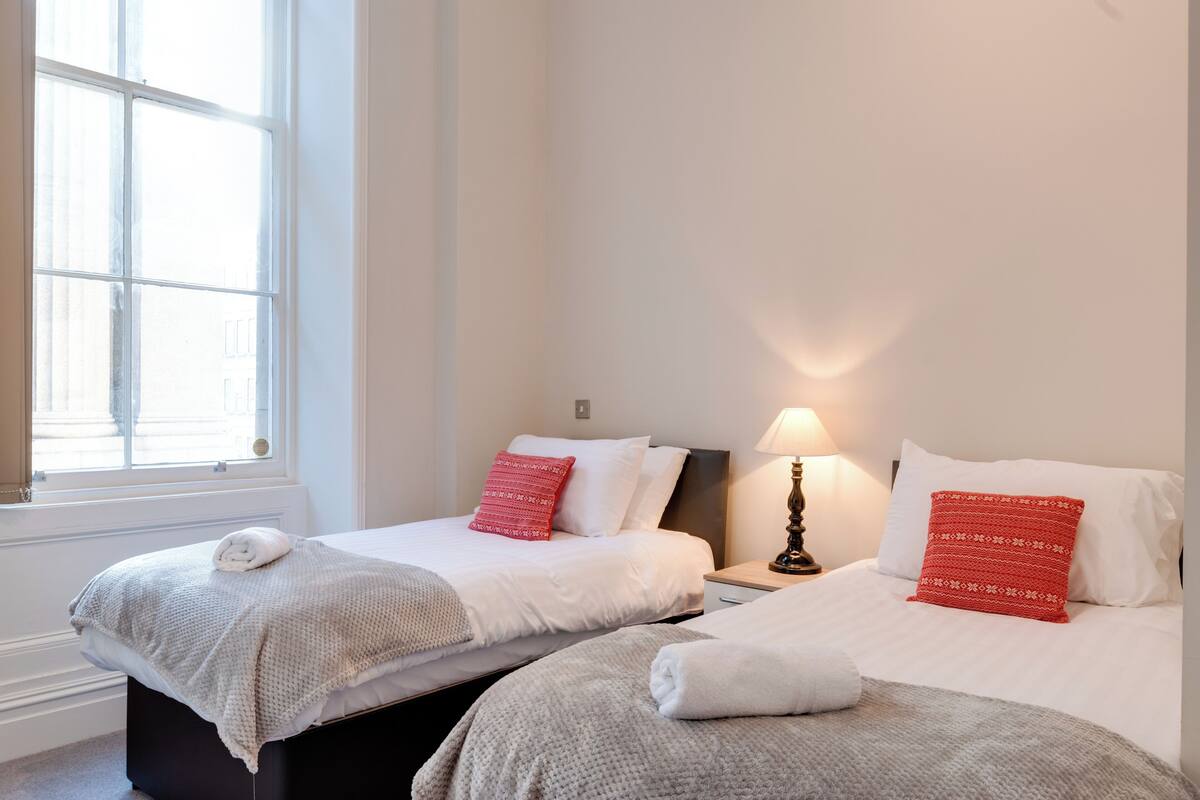 A hotel room with two beds, a window, and a nightstand with a lamp.