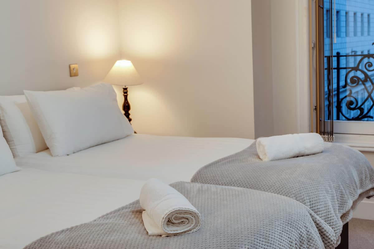 A hotel room with a bed, pillows, a lamp, a window with a view, and a towel.