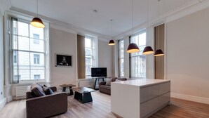 A spacious living area with a sofa, a coffee table, a TV, and pendant lights. - One by Elite  (Liverpool)