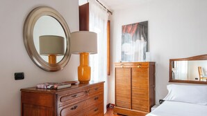 A bedroom with a wooden dresser, a bed with white linens, a round mirror, and a wooden wardrobe. - Panoramic Apartment Fori Imperiali (Rome)