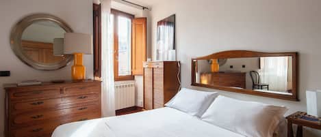 Un dormitorio con una cama, un aparador de madera, un espejo y una ventana con cortinas.