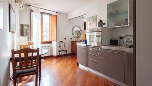 A modern kitchen with wooden flooring, a dining table with chairs, a built-in oven, and a microwave. - Panoramic Apartment Fori Imperiali (Rome)
