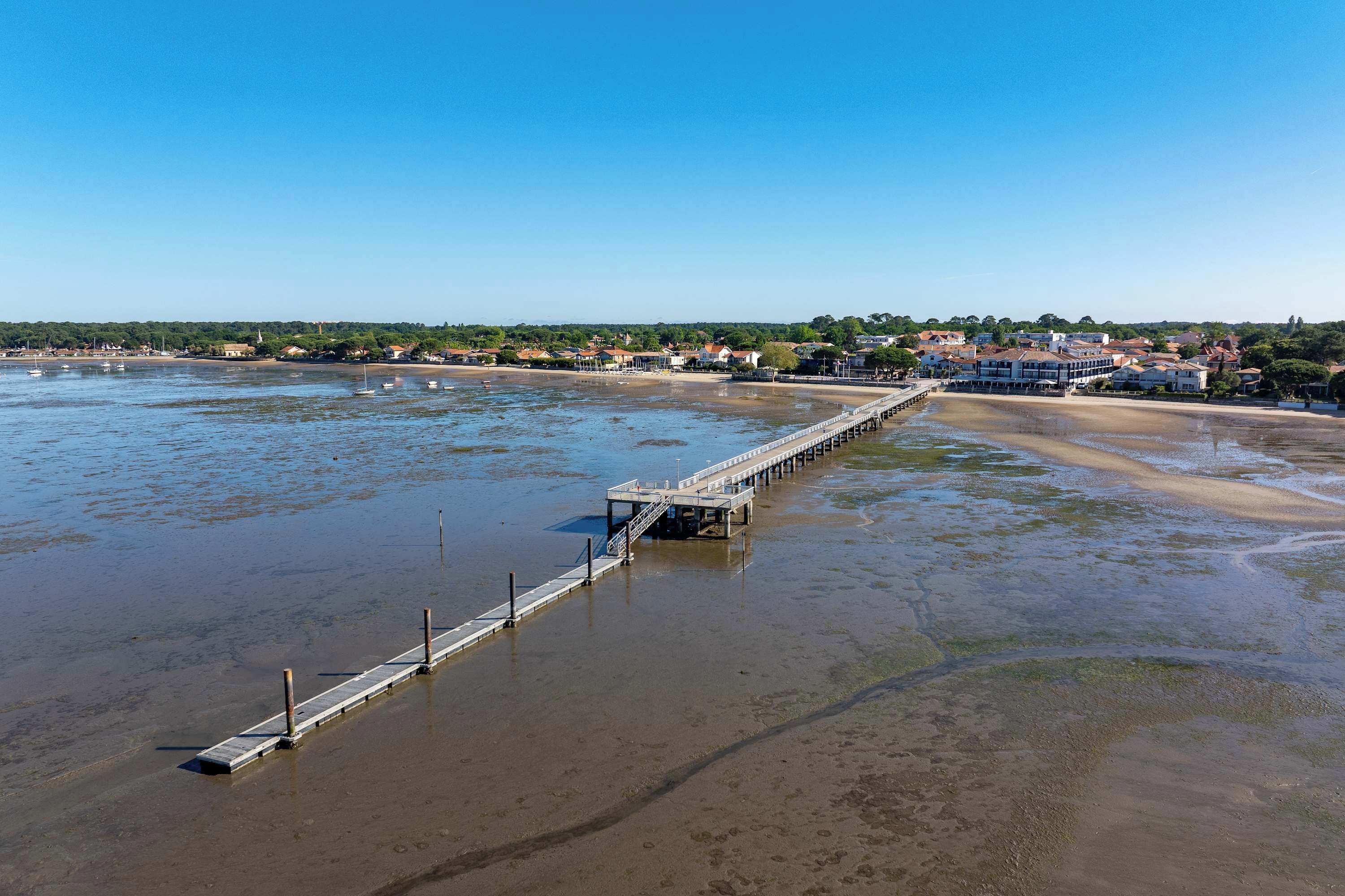 A coastal area with a pier extending into the water, a beach, and buildings in the background.