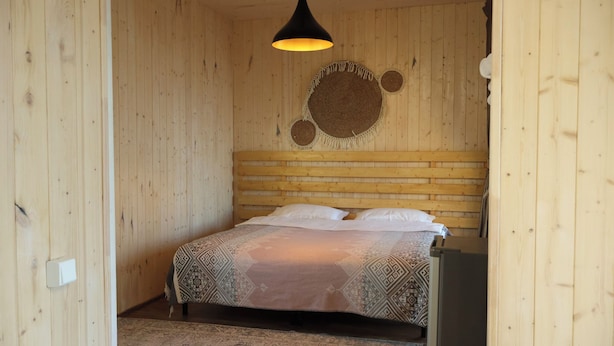 Ein Zimmer mit Holzboden, einem Bett, einer Hängeleuchte und einer gewebten Wanddekoration.