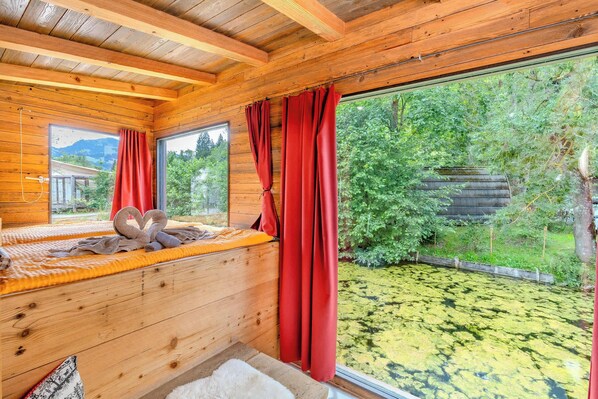 Habitación de cabaña de madera con un ventanal grande que da a un estanque y un bosque.