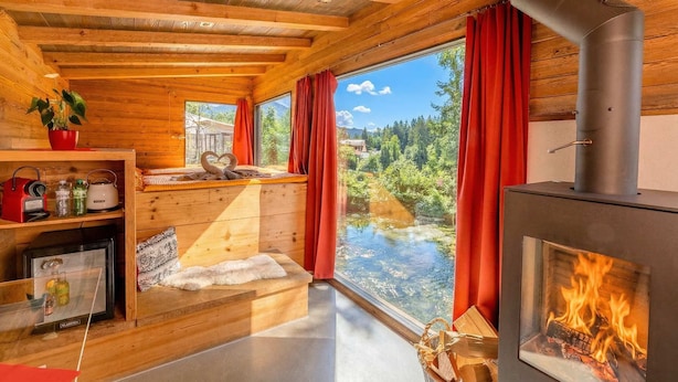 Ein Holzhäuschen im Inneren mit Kamin, einem Fenster mit Blick auf einen Wald und einer Küchenzeile mit Kochutensilien.